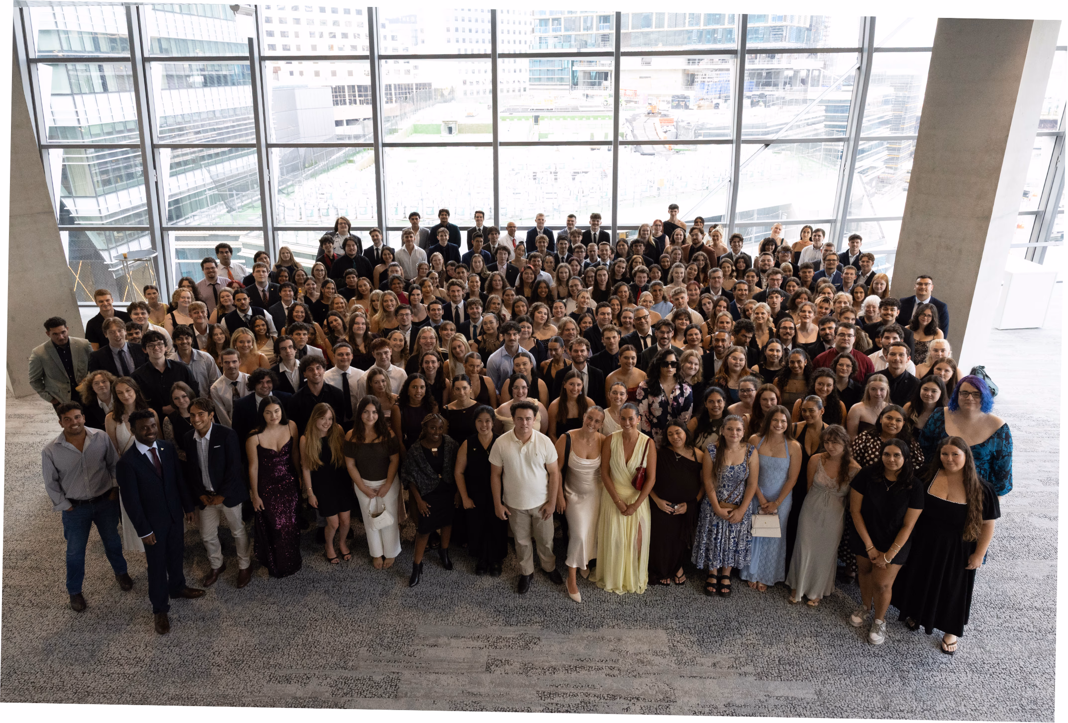 A large group of CareerTrackers students photographed together in the glass atrium of a corporate office tower.