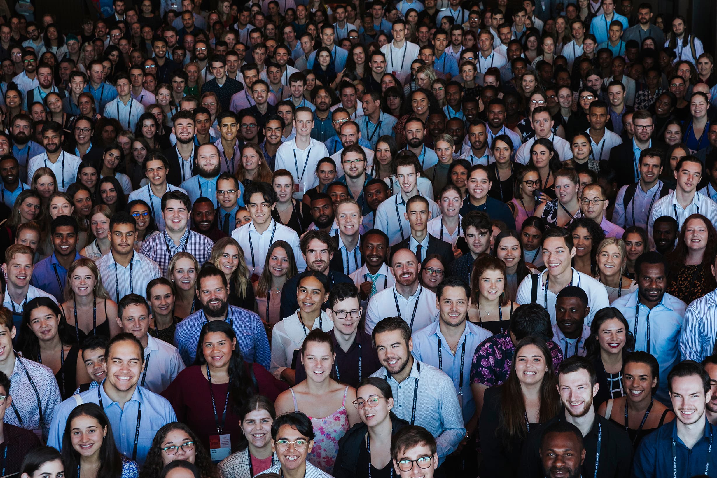 An aerial view of a large crowd of CareerTrackers students and alumni smiling together at a conference, wearing lanyards.