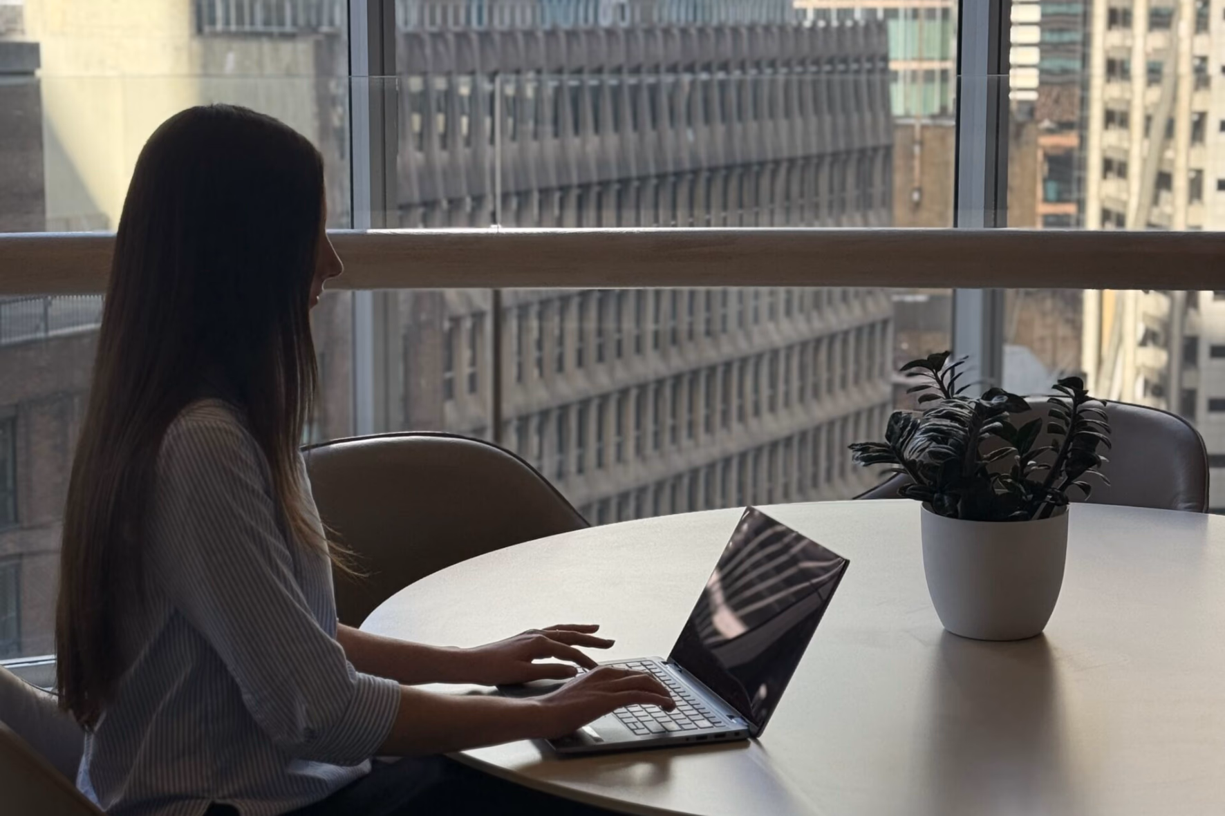 Samantha Colless working at a laptop in a meeting room overlooking the city